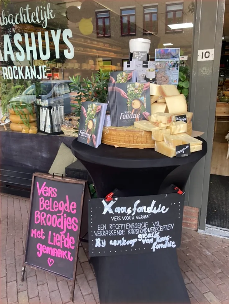 Statafel voor de winkel met kaas om te raspen, fondueboeken en het krijtbord Kaasfondue, vers voor u geraspt